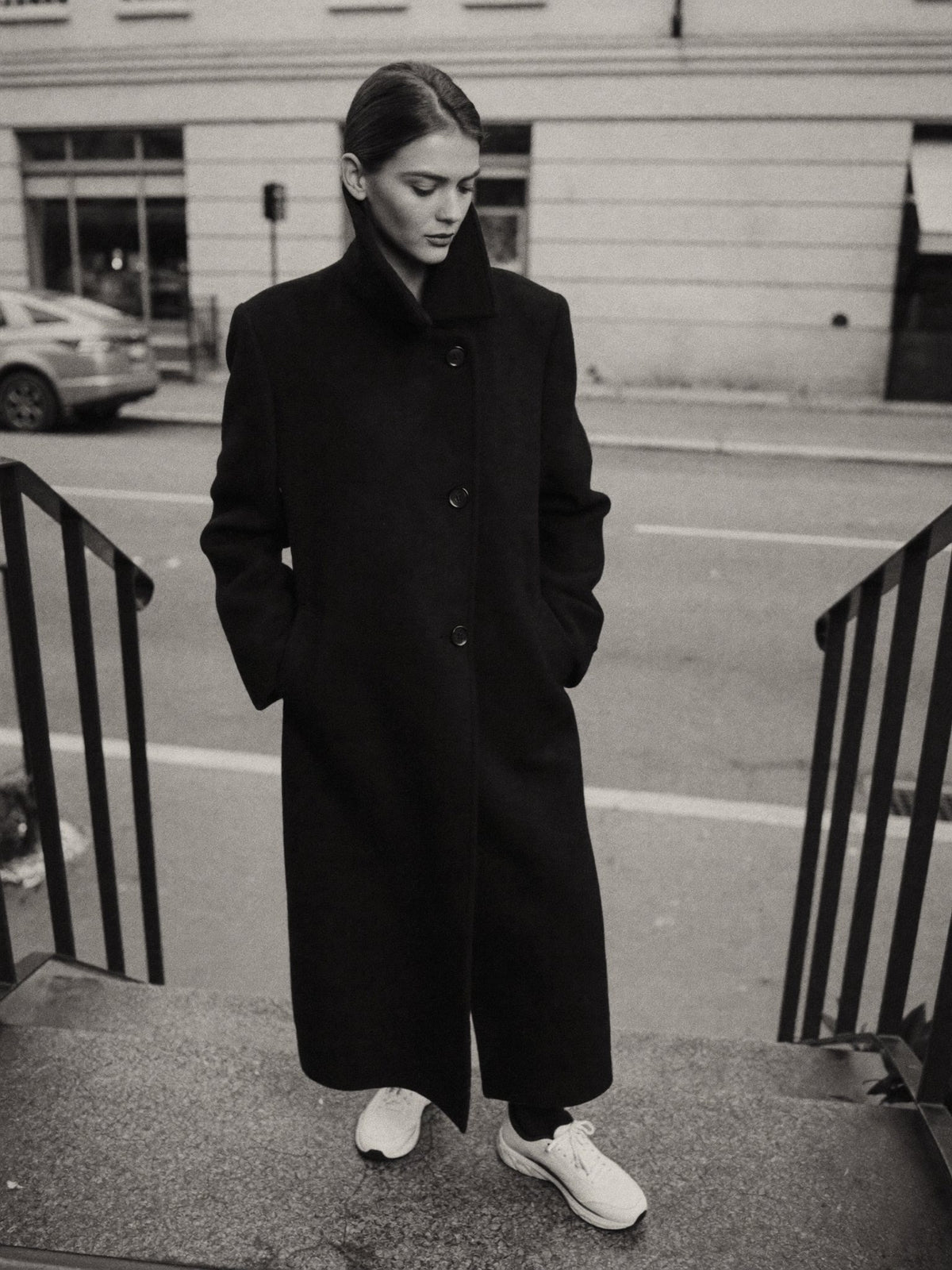 Woman in a winter coat and white sneakers sitting on stone steps